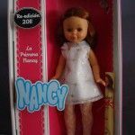 Nancys de colección: la Nancy de 1968. Foto de la muñeca dentro de la caja, tal cual se presenta, pero sin el plástico transparente de la tapa.. Esta reproducción es pelirroja, con los ojos color miel, marrones, y el vestido blanco con adornos dorados (flores) como el de la muñeca original