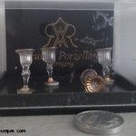 foto (primer plano en su caja) de las copas de cristal con filo y pie dorado de marca alemana que me han regalado para mi casa de muñecas, junto a una peseta para apreciar la escala